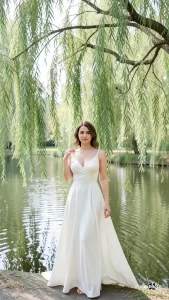 保持女性人物完全不变，保留面部、发型和服装。仅调整体态使胸部更开阔，保留柳树和水池背景。